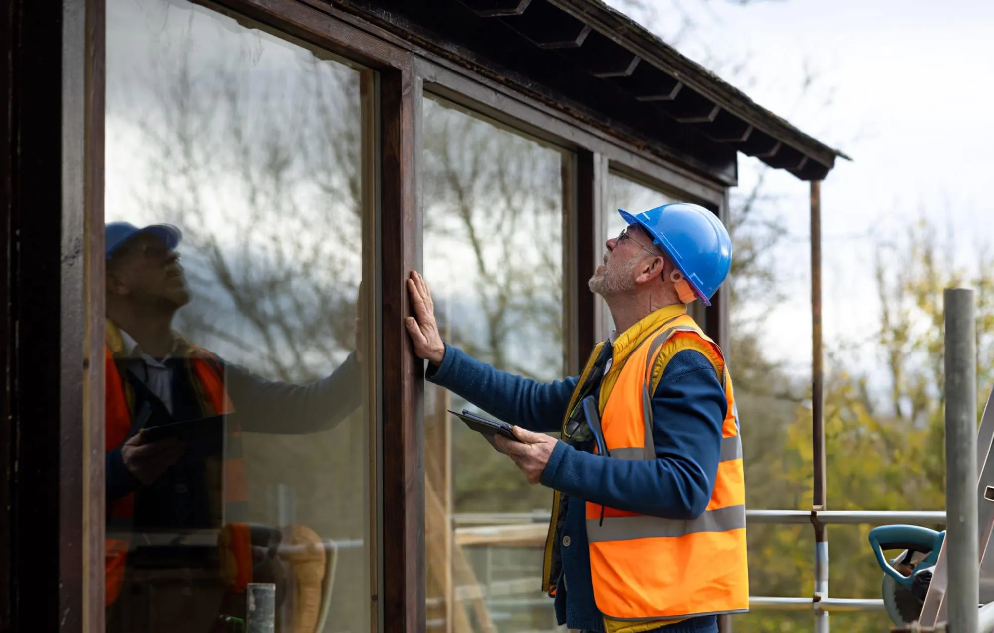 Construction worker in a hard hat and orange vest inspecting a window frame on a building under construction