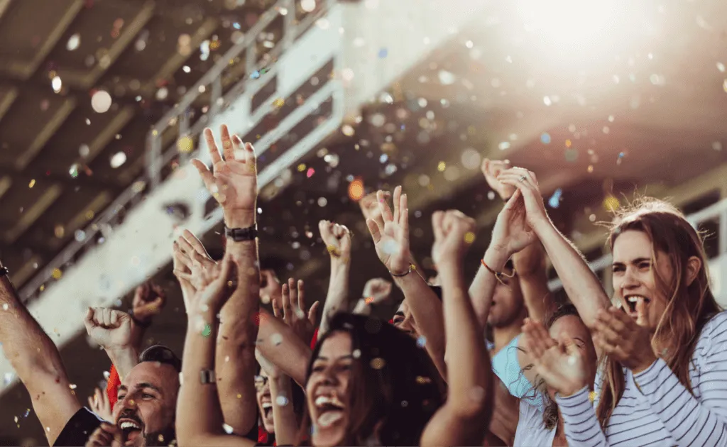 Cheering sports fans with raised arms in a stadium as confetti falls