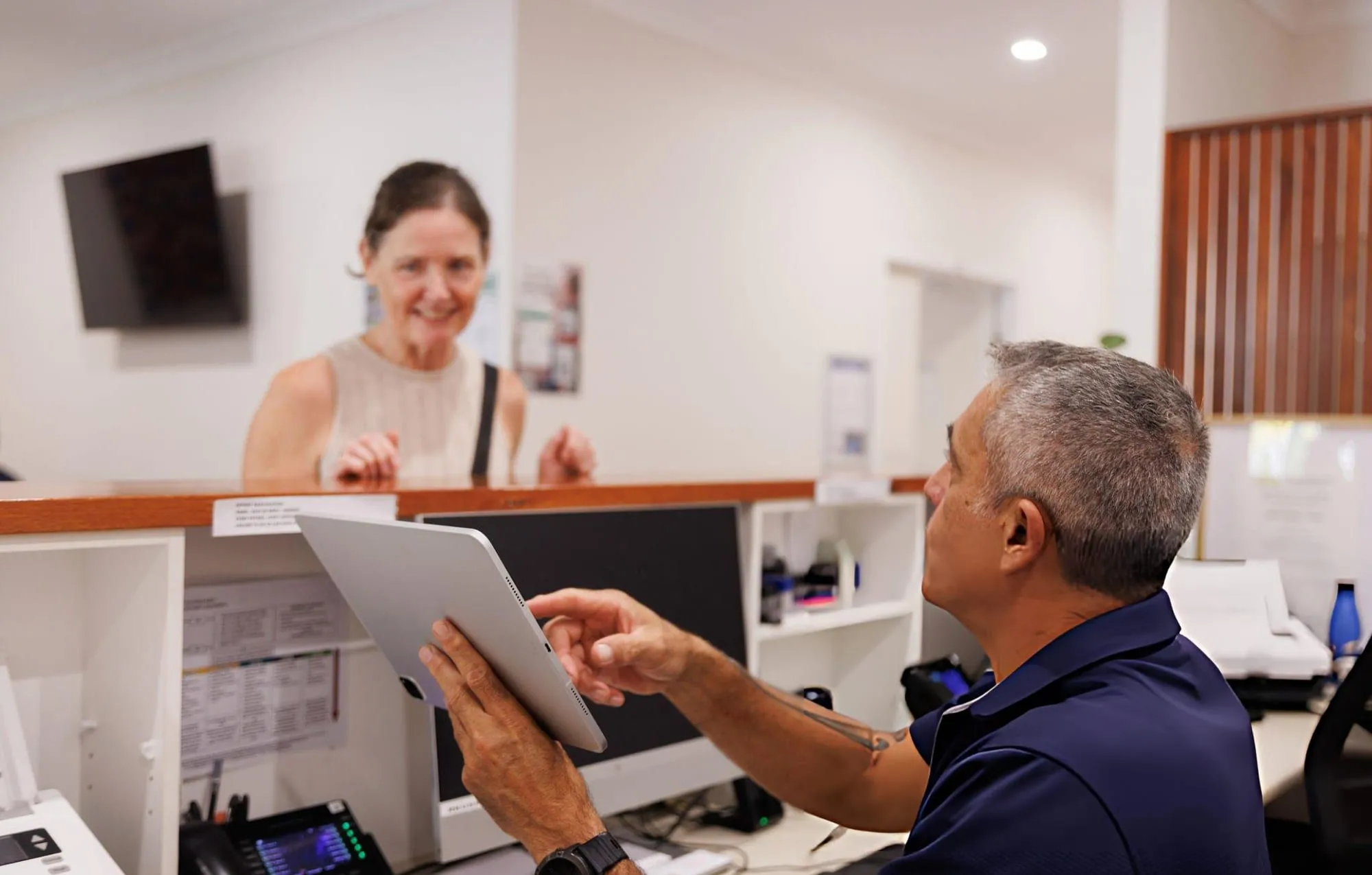 Staff member at a service counter pointing at a tablet while a smiling customer looks on