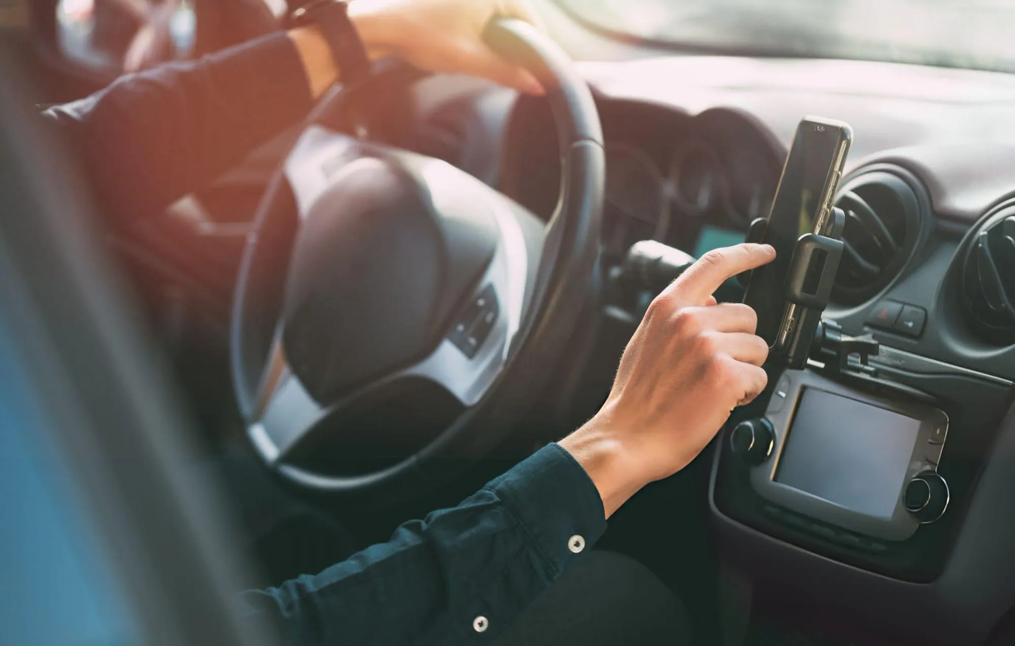 Driver's hand touching a phone mounted on a truck dashboard while the other hand holds the wheel