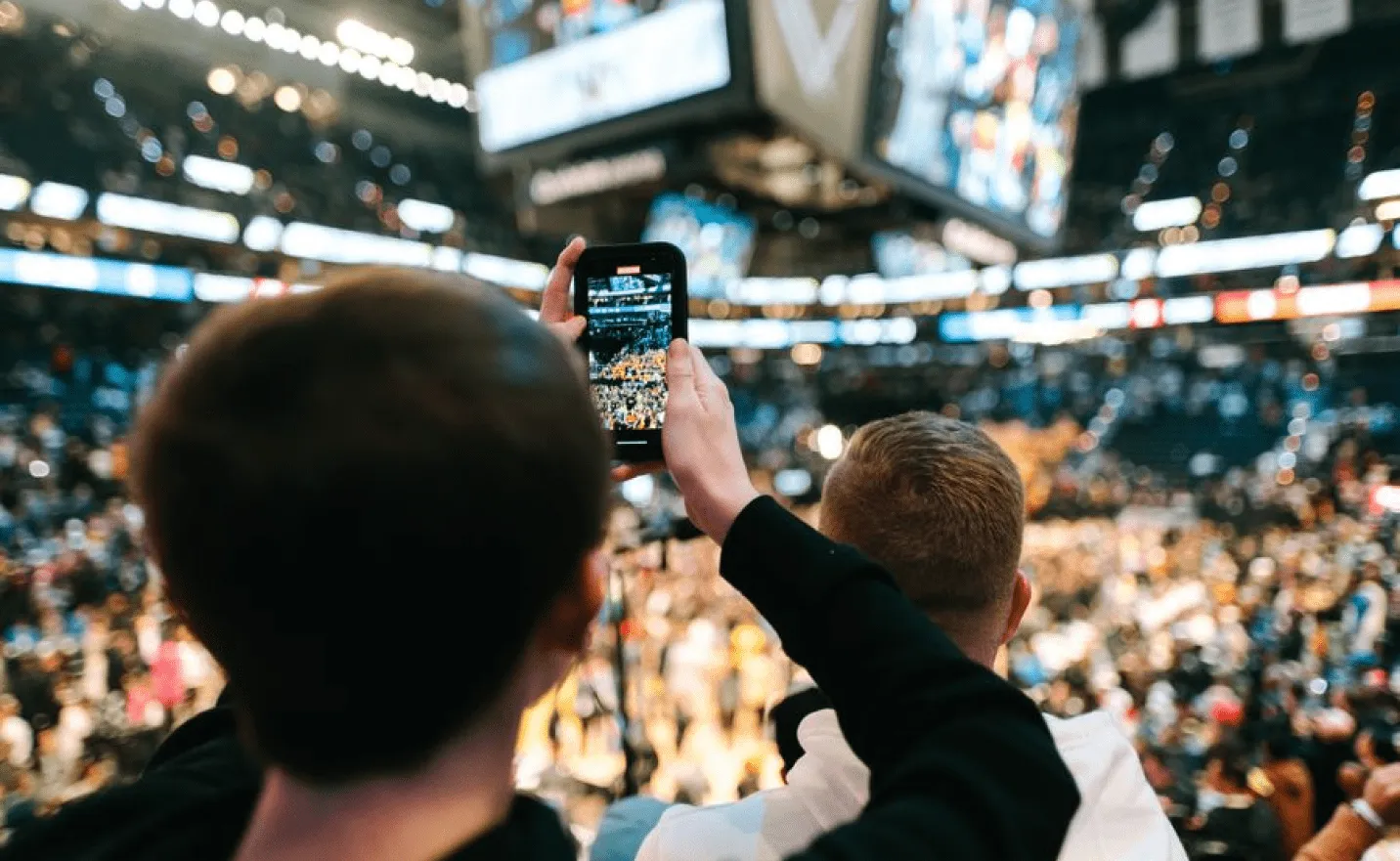 Fan holding up a phone to film a packed arena from the stands