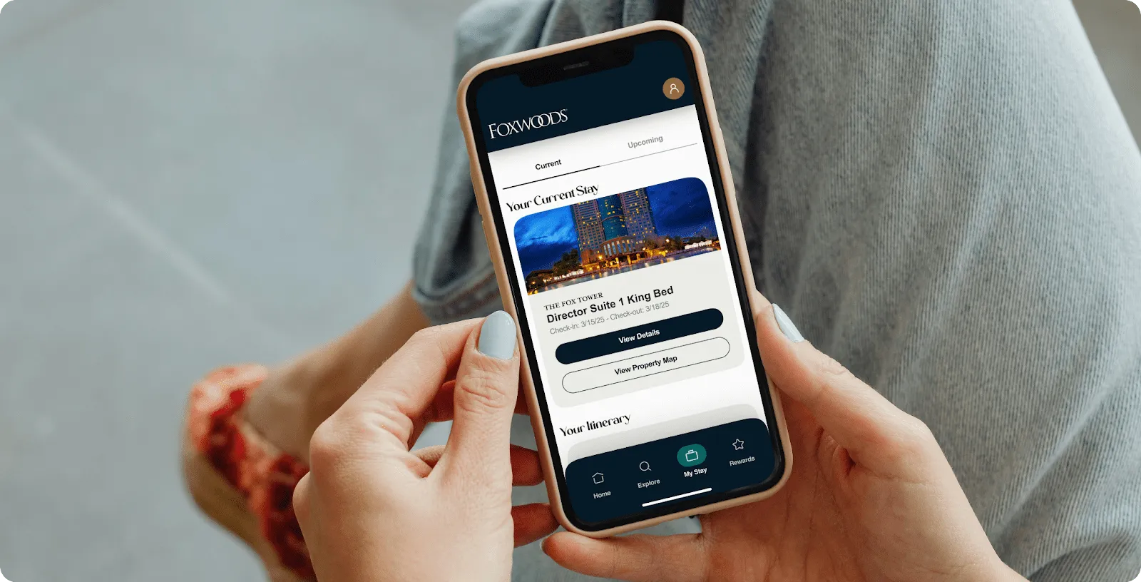 Hands holding a phone showing the Foxwoods app My Stay screen with a current hotel booking