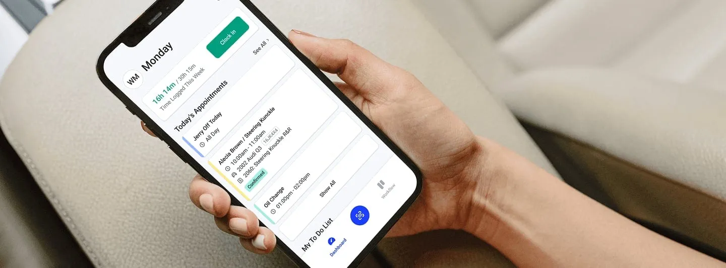 A hand holding a phone that shows a technician's daily appointments in the Shopmonkey app.
