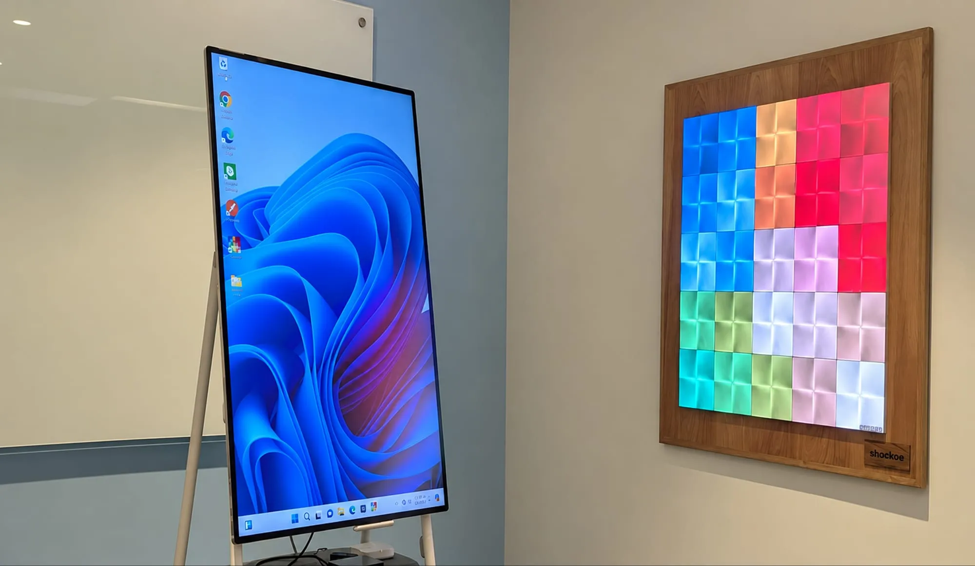 A wall display of colorful light panels in a wooden frame beside a tall screen in a meeting room.