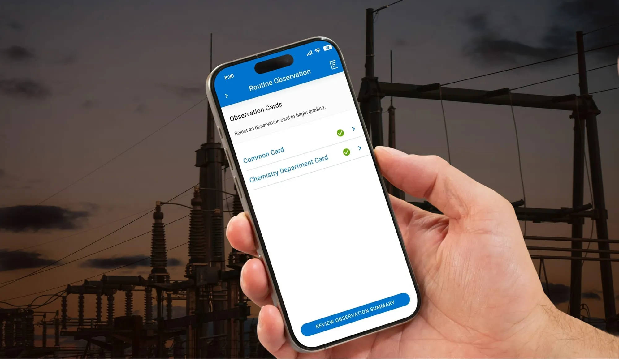 A hand holding a phone that shows a list of observation cards, with electrical equipment against a dusk sky behind it.