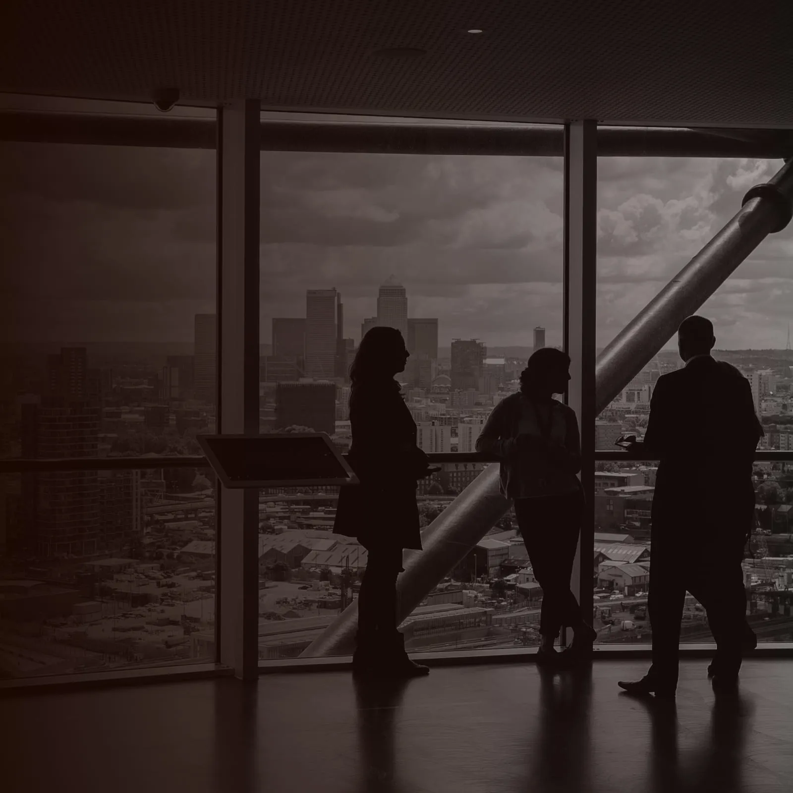 Three colleagues in silhouette talking beside a window with a city skyline behind them.