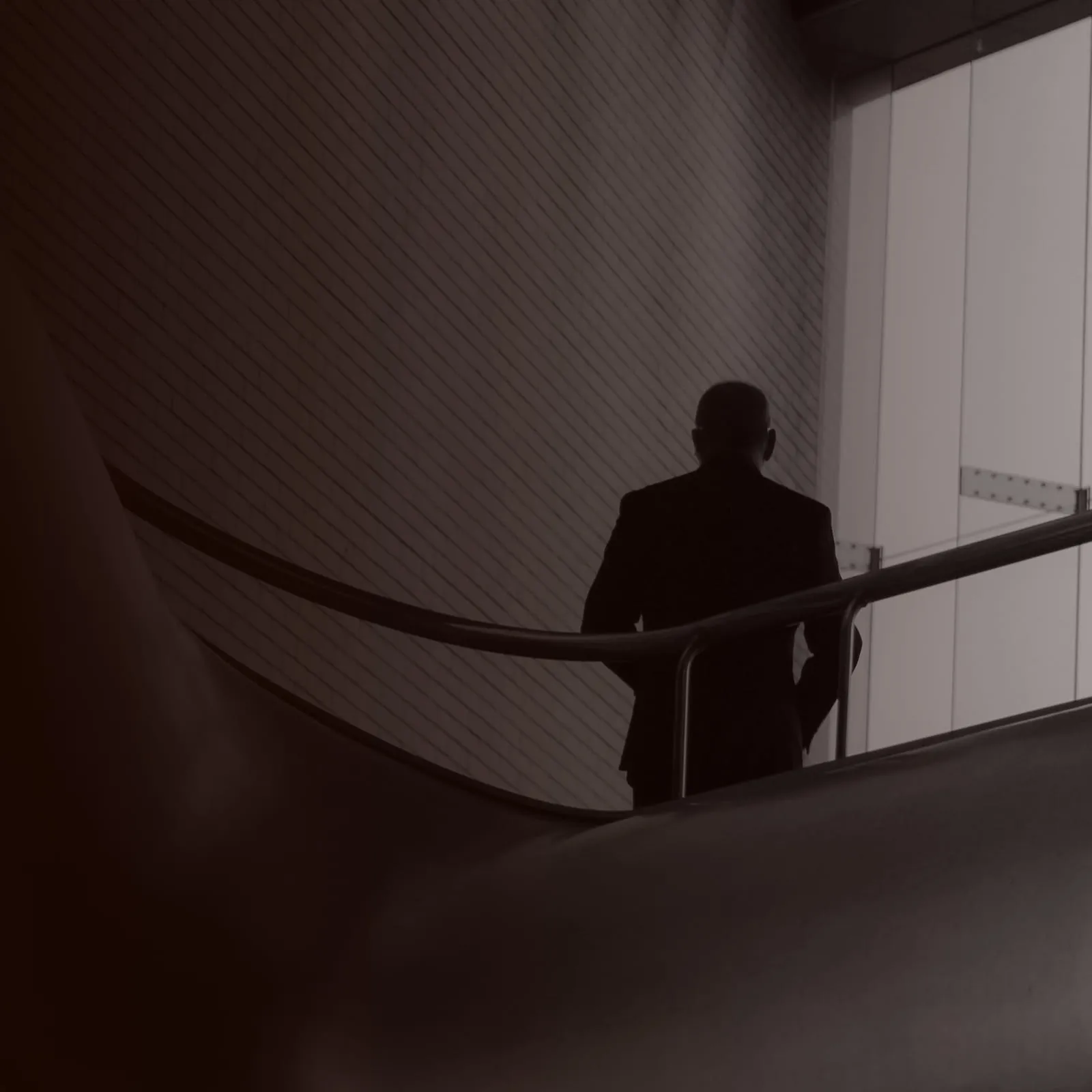 A person in a suit seen from behind, standing at a curved stair railing.