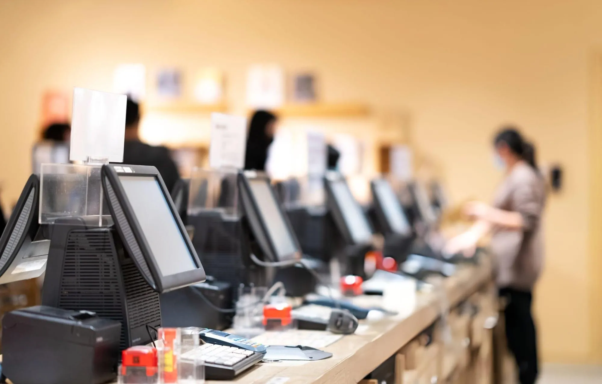 Row of point-of-sale terminals on a retail counter with blurred staff behind