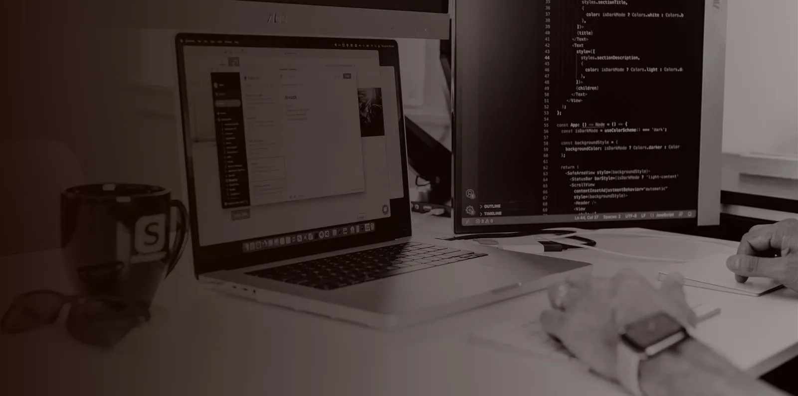 A developer's desk with a laptop, a monitor showing code, and a mug with the Shockoe logo.