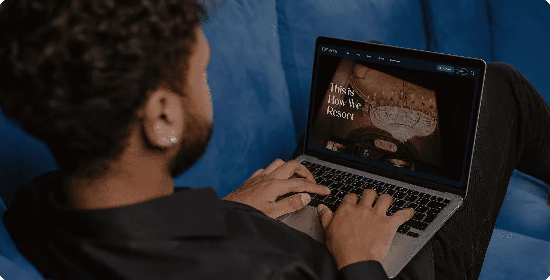Person lying on a blue sofa typing on a laptop that shows the Foxwoods website home page
