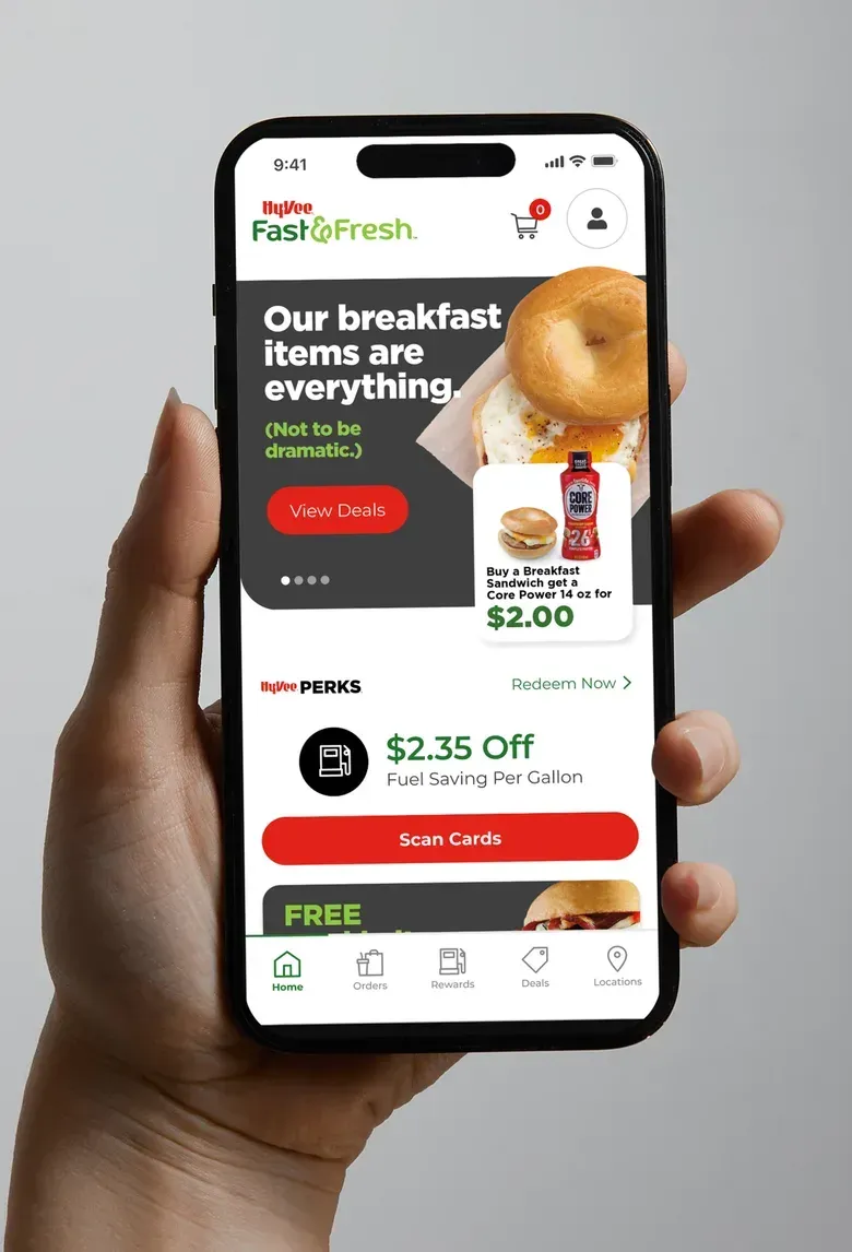 A hand holding a phone showing the Fast & Fresh app home screen with a breakfast promotion and a rewards card.