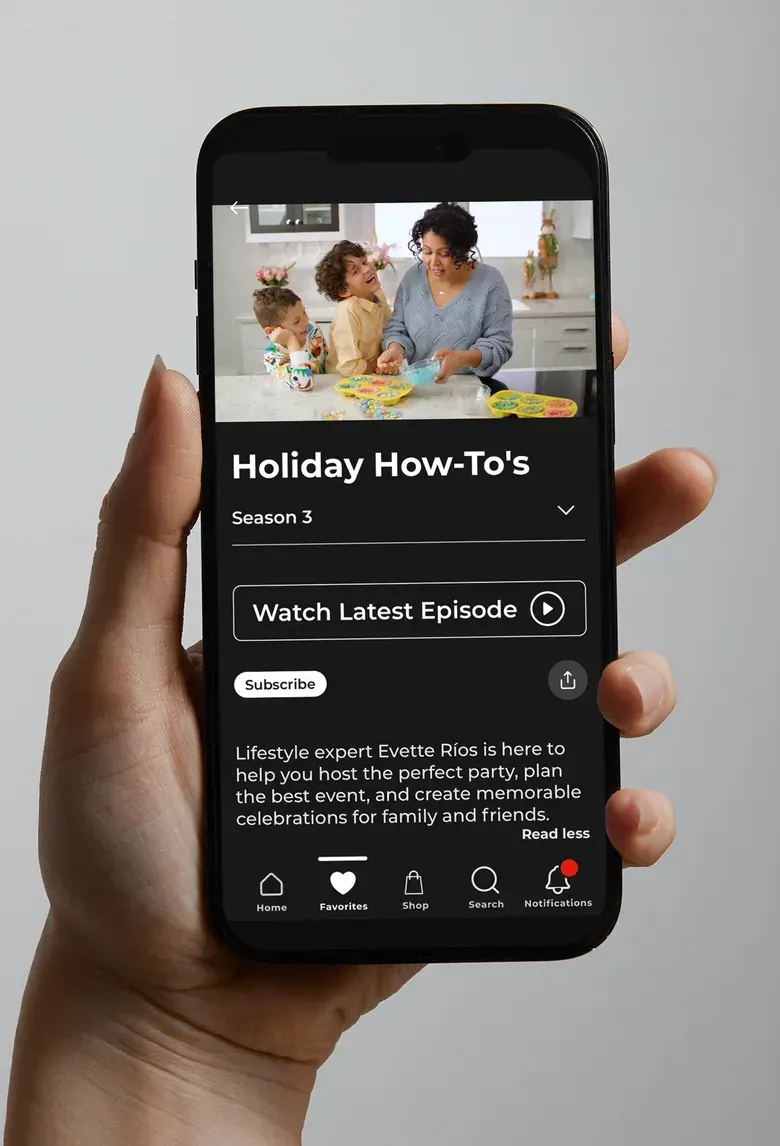 A hand holding a phone showing an HSTV show page titled Holiday How-Tos with a Watch Latest Episode button and a Subscribe button.