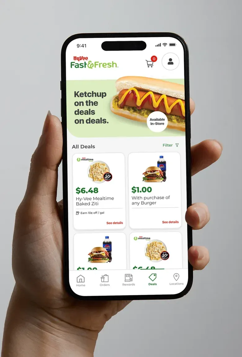 A hand holding a phone showing the Fast & Fresh All Deals screen with a hot dog promotion and a list of deals.