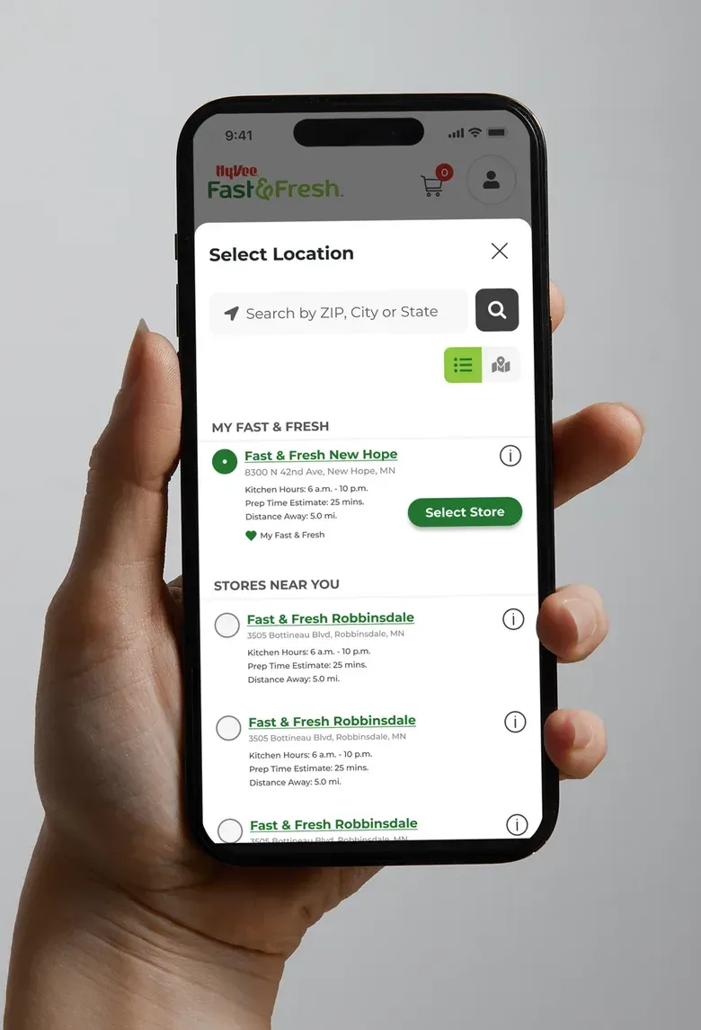 A hand holding a phone showing the Fast & Fresh Select Location screen with a list of nearby stores.