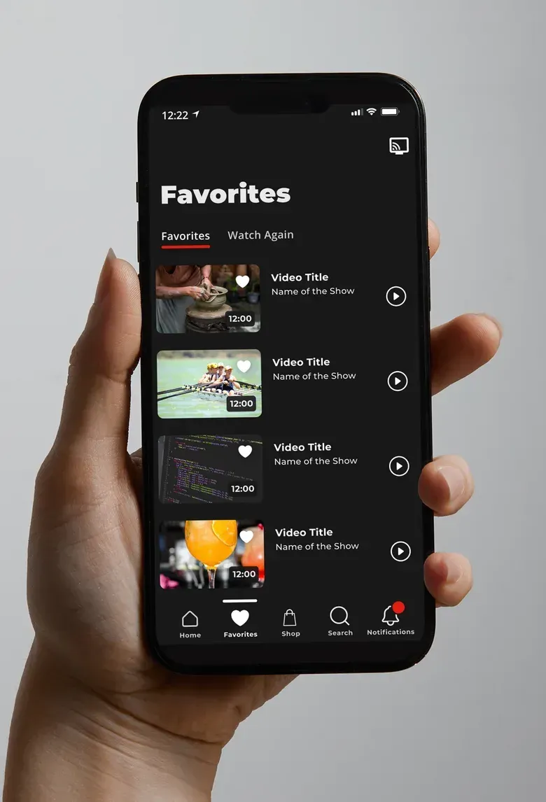 A hand holding a phone showing the HSTV Favorites screen, a list of saved videos with play buttons.