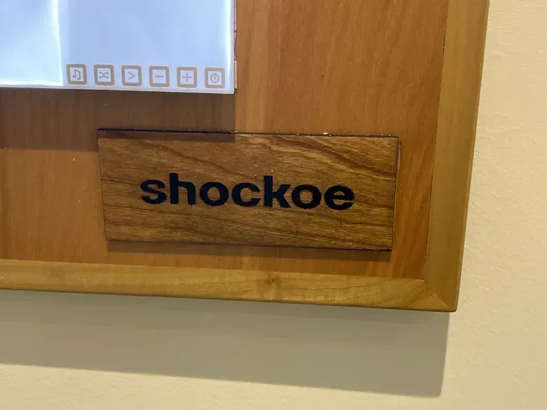 A close view of the frame corner with a wooden nameplate and the touch controls of a light panel.