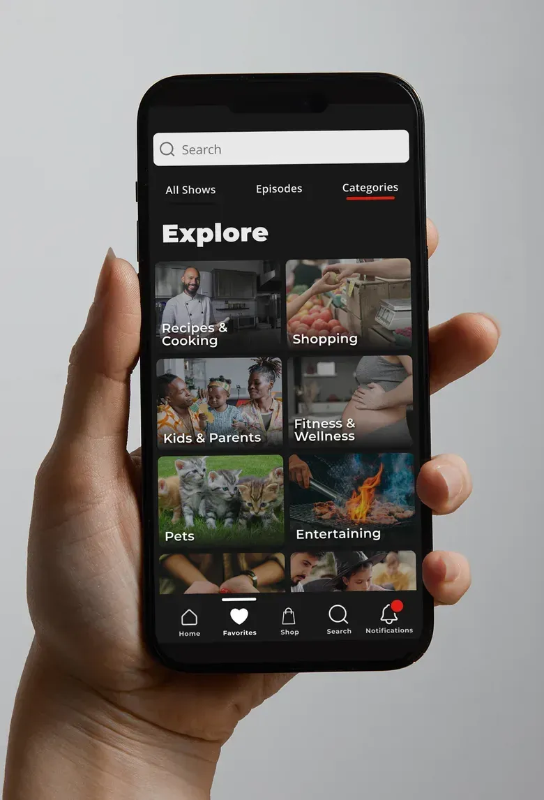 A hand holding a phone showing the HSTV Explore screen, a grid of categories such as Recipes and Cooking, Kids and Parents, and Entertaining.