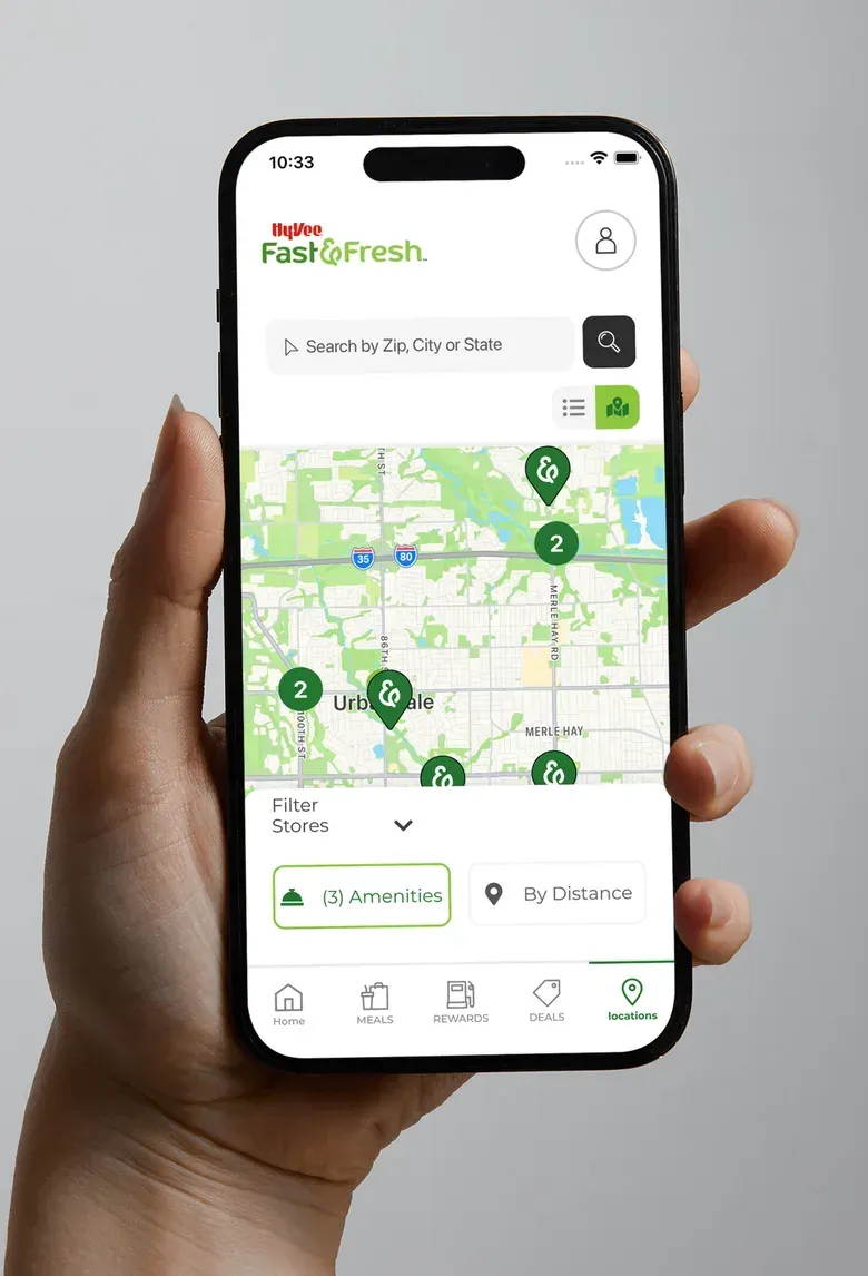 A hand holding a phone showing the Fast & Fresh store finder with a map and numbered pins.