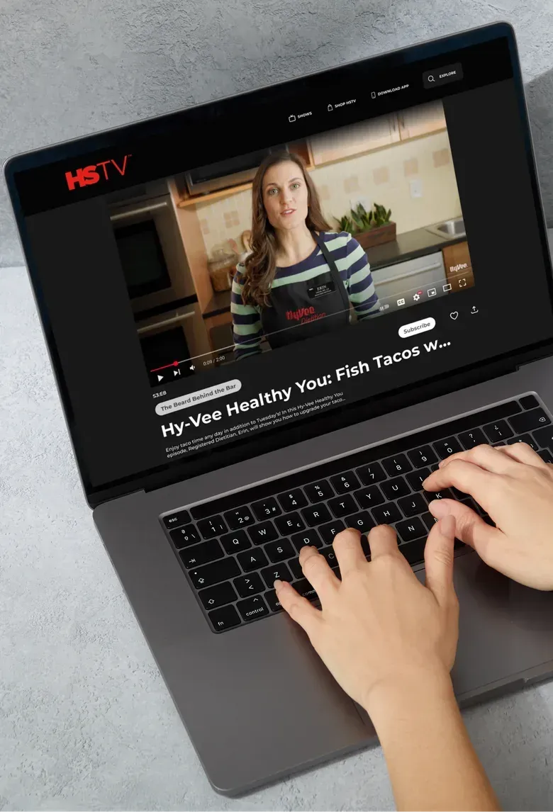 A laptop showing the HSTV web app playing a cooking video with the episode title below the player.