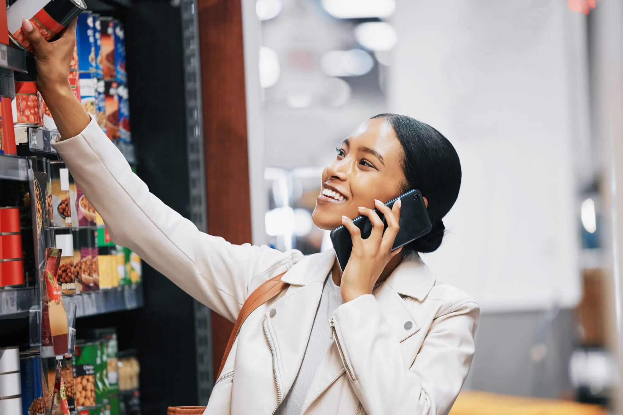 Smiling shopper on a phone call reaching for a product on a store shelf